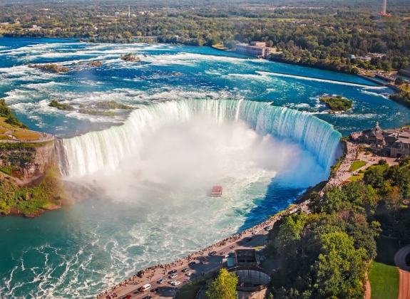 Aerial top landscape view of Niagara Falls and tour boat in water between US and Canada.  Horseshoe of famous Canadian waterfall on sunny day
