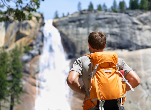 Hiker hiking with backpack looking at waterfall in Yosemite park in beautiful summer nature landscape. Portrait of male adult back standing outdoor.