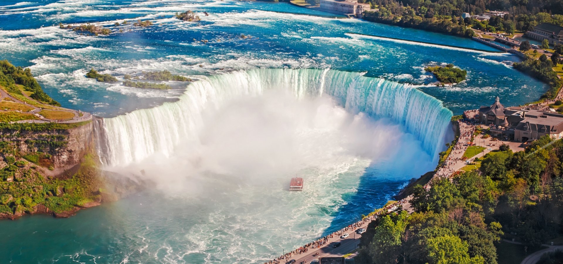 Aerial top landscape view of Niagara Falls and tour boat in water between US and Canada.  Horseshoe of famous Canadian waterfall on sunny day