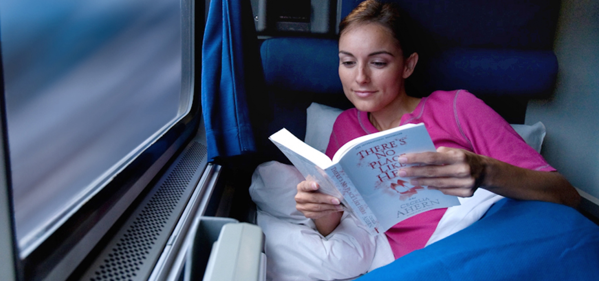 a woman reading a book in a private Amtrak Roomette